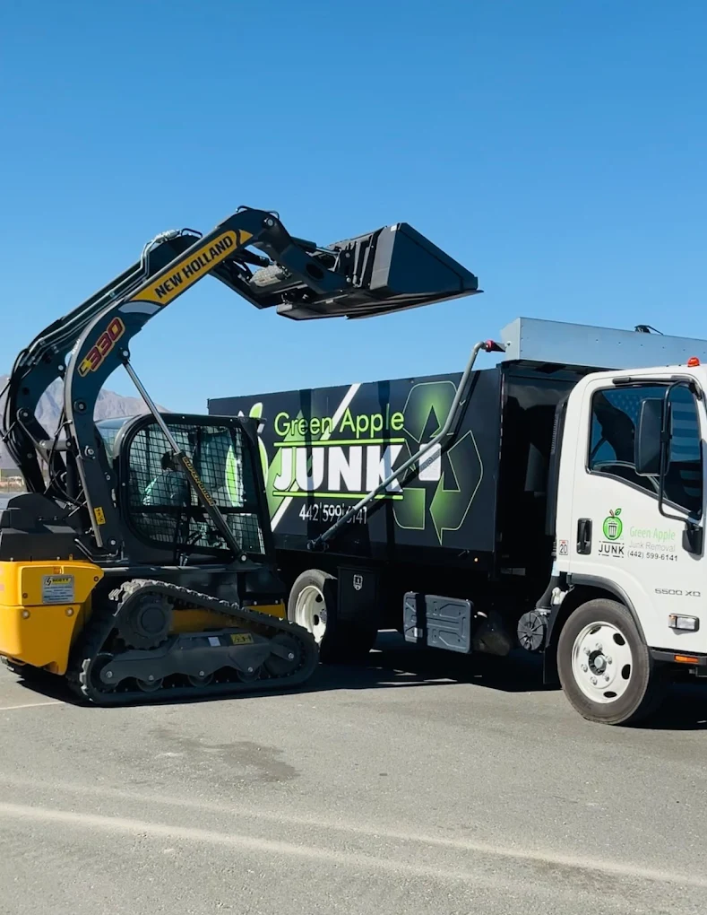 New Holland skid steer loading into Green Apple junk truck — full equipment shot